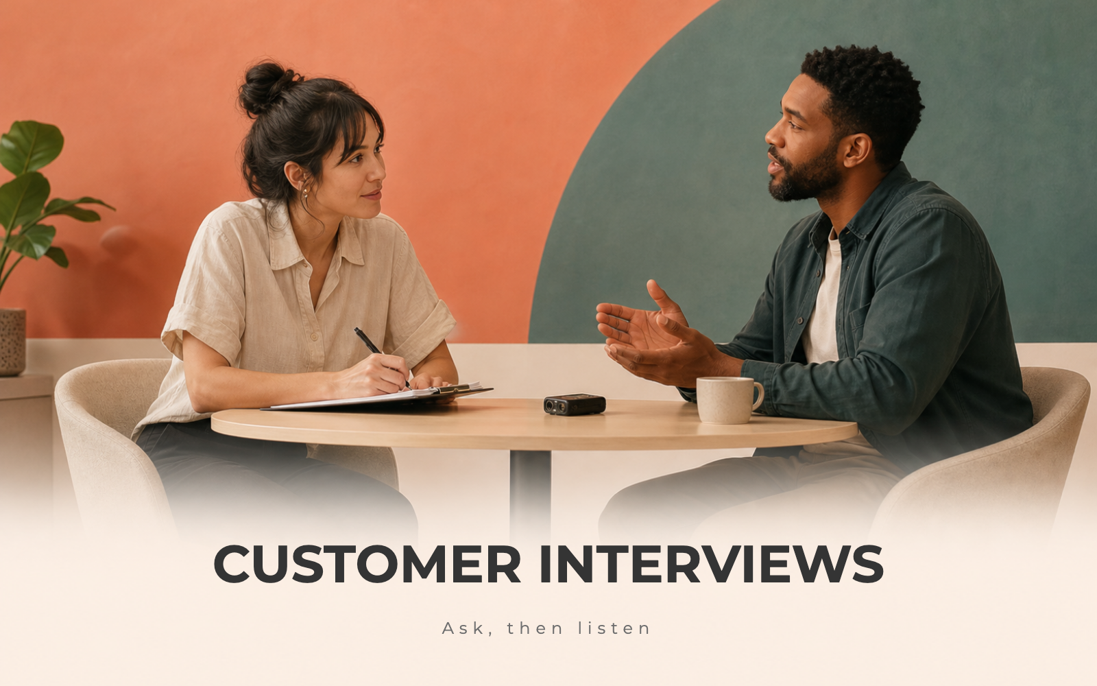 Two people in a customer interview across a table, one taking notes with a recorder between them